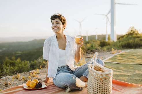 Lächelnde Frau mit Saftglas auf einem Berg sitzend beim Picknick - GMCF00208