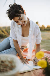 Frau lächelt, während sie beim Picknick in ein Buch schreibt - GMCF00220