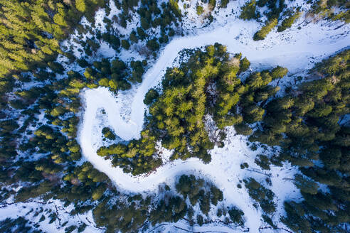 Luftaufnahme einer verschneiten Straße in einem Wald, während des Sonnenuntergangs, Fieberbrunn, Tirol, Österreich. - AAEF12542