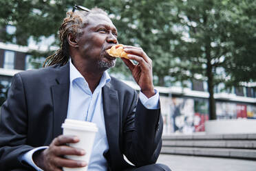 Geschäftsmann mit Einwegbecher isst Croissant - ASGF00897