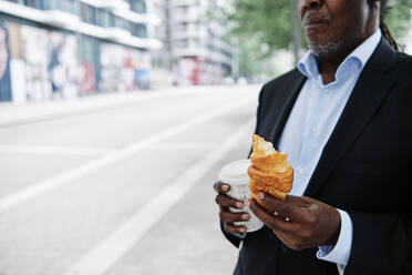 Männlicher Berufstätiger mit Croissant und Kaffeetasse - ASGF00901