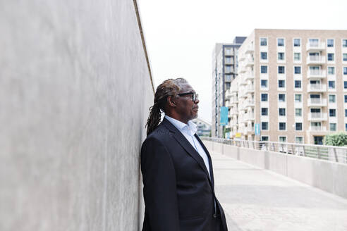 Thoughtful businessman standing in front of gray wall - ASGF00904