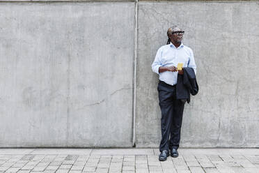 Businessman holding mobile phone while standing on footpath - ASGF00910