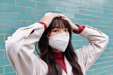 Frau mit Kopf in den Händen, die während einer Pandemie eine Schutzmaske trägt - ASGF00959