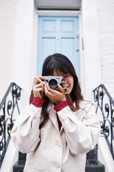 Junge Frau fotografiert mit analoger Kamera vor einem Gebäude - ASGF00984