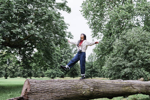 Carefree young woman balancing on log in public park - ASGF00987