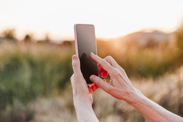 Ältere Frau benutzt ihr Smartphone beim Wandern während des Sonnenuntergangs - EBBF04401