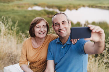 Smiling mother and son taking selfie near lake - EBBF04410