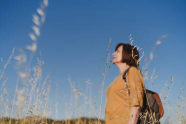 Frau mit Rucksack steht vor blauem Himmel - EBBF04412