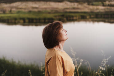 Senior woman with eyes closed at lakeshore - EBBF04413