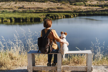 Woman with dog sitting on bench near lake - EBBF04414