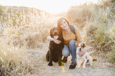Woman embracing dogs while crouching on trail - EBBF04430