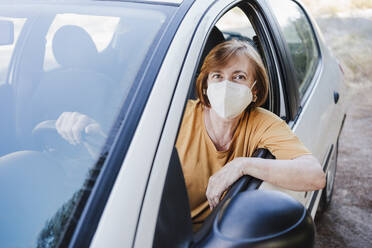 Senior woman with protective face mask sitting in car during COVID-19 - EBBF04433