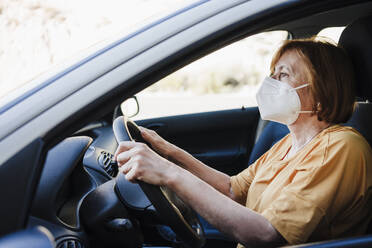 Frau mit Gesichtsschutzmaske beim Autofahren während COVID-19 - EBBF04434