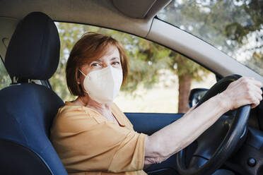 Frau im Auto mit Gesichtsschutzmaske während COVID-19 - EBBF04435