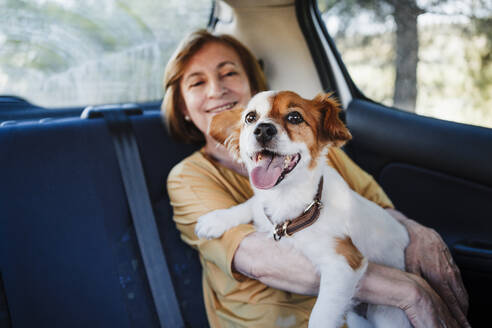 Ältere Frau mit Hund im Auto sitzend - EBBF04437