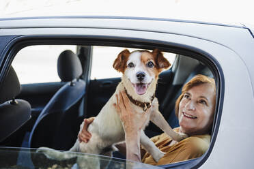 Woman looking at pet dog while sitting in car - EBBF04438