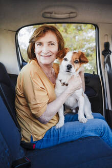 Frau sitzt mit Hund auf dem Rücksitz eines Autos - EBBF04439