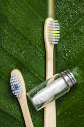 Zahnbürsten aus Holz und biologisch abbaubare Zahnseide auf grünem Blatt liegend - FLMF00620