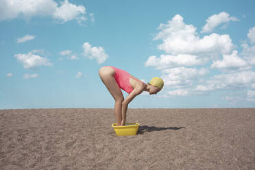 Woman bending in bucket on sand at beach - VPIF04444