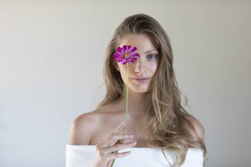 Junge Frau in schulterfreiem Top bedeckt Auge mit lila Gänseblümchen - EIF01794