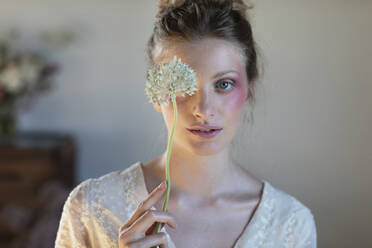 Young blond woman covering eye with allium flower - EIF01814