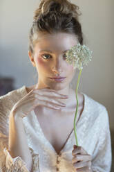 Junge Frau mit Hand am Kinn, die eine Alliumblüte in einem Atelier hält - EIF01816