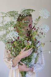 Young woman cover face with wild flowers in front of white background - EIF01831