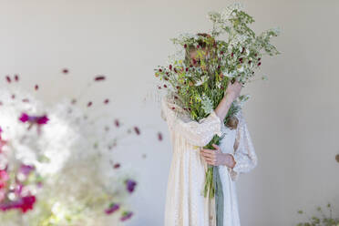 Bedecktes Gesicht einer Frau mit Wildblumenstrauß im Studio - EIF01833