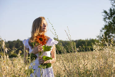 Schöne junge Frau mit geschlossenen Augen und Sonnenblume im Feld - EIF01838