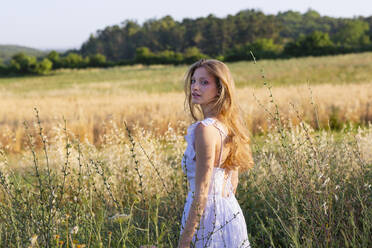 Beautiful woman in white dress standing amidst plants in field - EIF01843