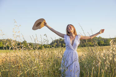 Fröhliche junge Frau mit Hut inmitten von Gras auf einem Feld - EIF01844