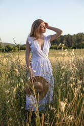 Beautiful woman holding straw hat amidst plants in field - EIF01847