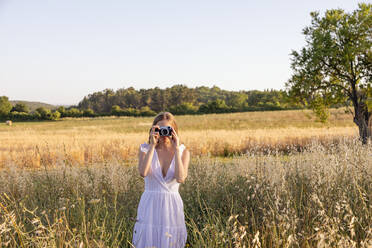 Junge Frau, die durch eine Kamera im Feld fotografiert - EIF01850
