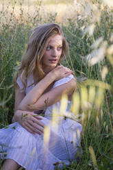 Beautiful woman looking away while sitting amidst grass in field - EIF01854