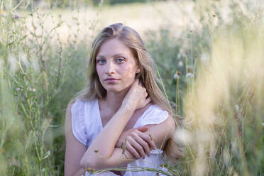 Beautiful young woman sitting amidst grass in field - EIF01856