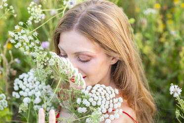 Lächelnde Frau mit geschlossenen Augen, die an Blumen riecht - EIF01873