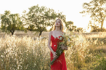 Junge schöne Frau mit geschlossenen Augen, die einen Strauß Wildblumen auf einem Feld hält - EIF01876