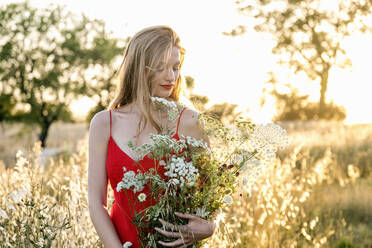 Beautiful woman in red dress holding flowers in field - EIF01878