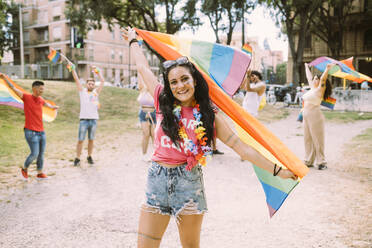 Lächelnde Frau mit Regenbogenfahne bei Pride-Event im Park - MEUF03634