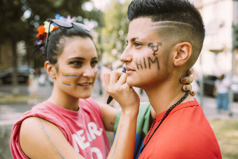 Woman writing on transgender friend's face during pride event - MEUF03642