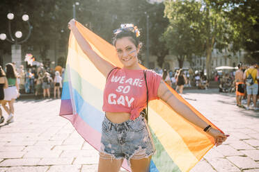 Young female protester with rainbow flag on footpath - MEUF03662