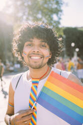 Lächelnder männlicher Demonstrant mit Regenbogenfahne bei einer Pride-Veranstaltung - MEUF03665