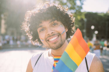 Männlicher Aktivist mit Regenbogenfahne bei einer Pride-Veranstaltung an einem sonnigen Tag - MEUF03666