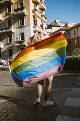 Junge Aktivistin mit Regenbogenfahne auf der Straße an einem sonnigen Tag - MEUF03686