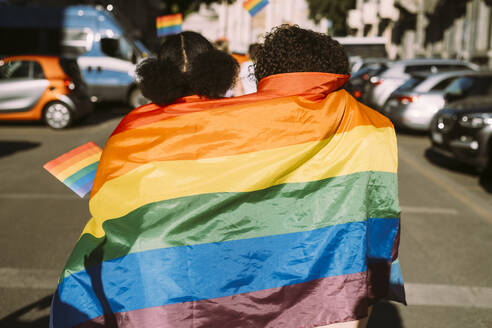 Female friends wrapped in rainbow flag on sunny day - MEUF03702