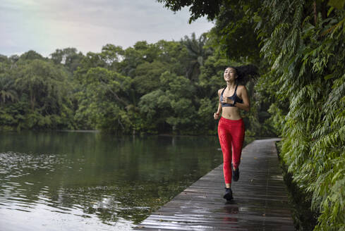 Smiling young woman running on boardwalk by lake - EAF00026