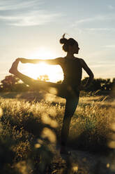 Woman doing stretching exercise at countryside during sunset - DAMF00893