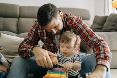 Father teaching xylophone to son in living room - GMCF00228