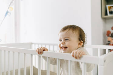 Smiling baby boy looking away in crib at home - GMCF00233